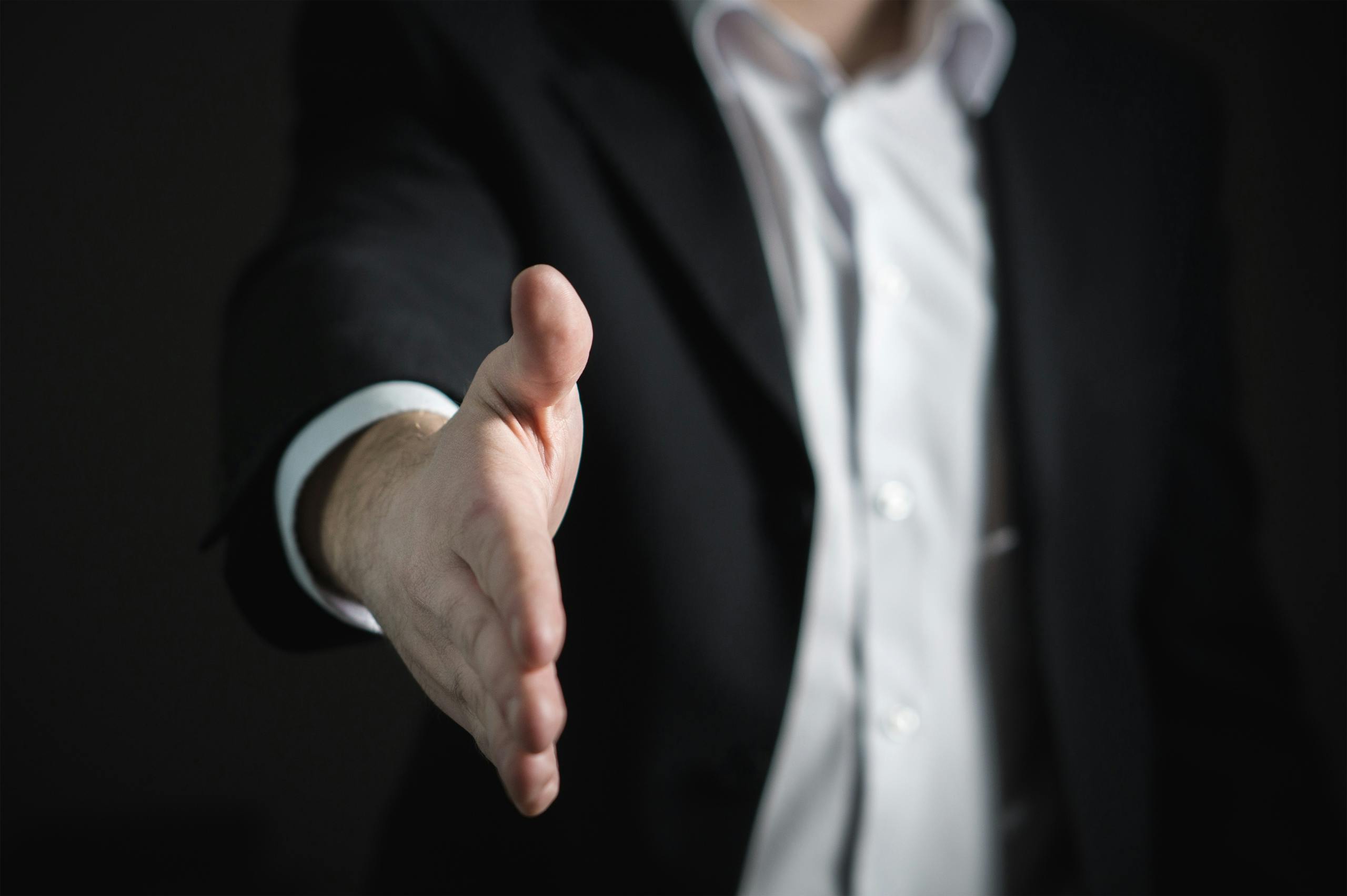Usluge 1 Close-up of a businessman extending hand for a handshake, symbolizing agreement and partnership.
